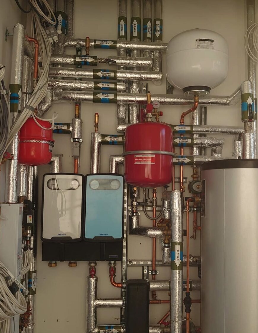 Plant room in a Connaught Square flat with labelled insulated pipework, expansion vessels, pump groups and cylinder